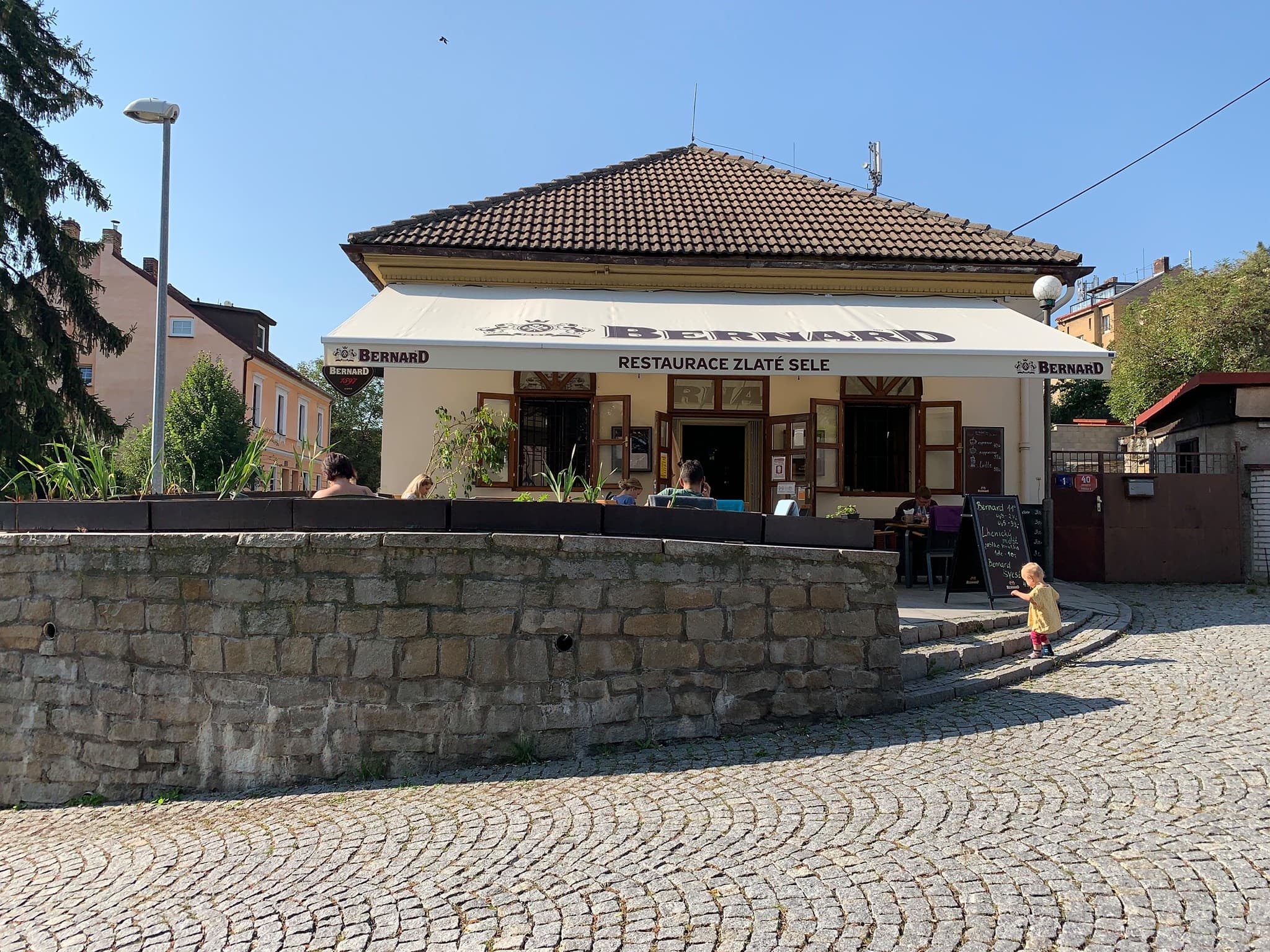 Restaurace Zlaté Sele — rohový dům se zahrádkou na dlážděné ulici Starého Proseka